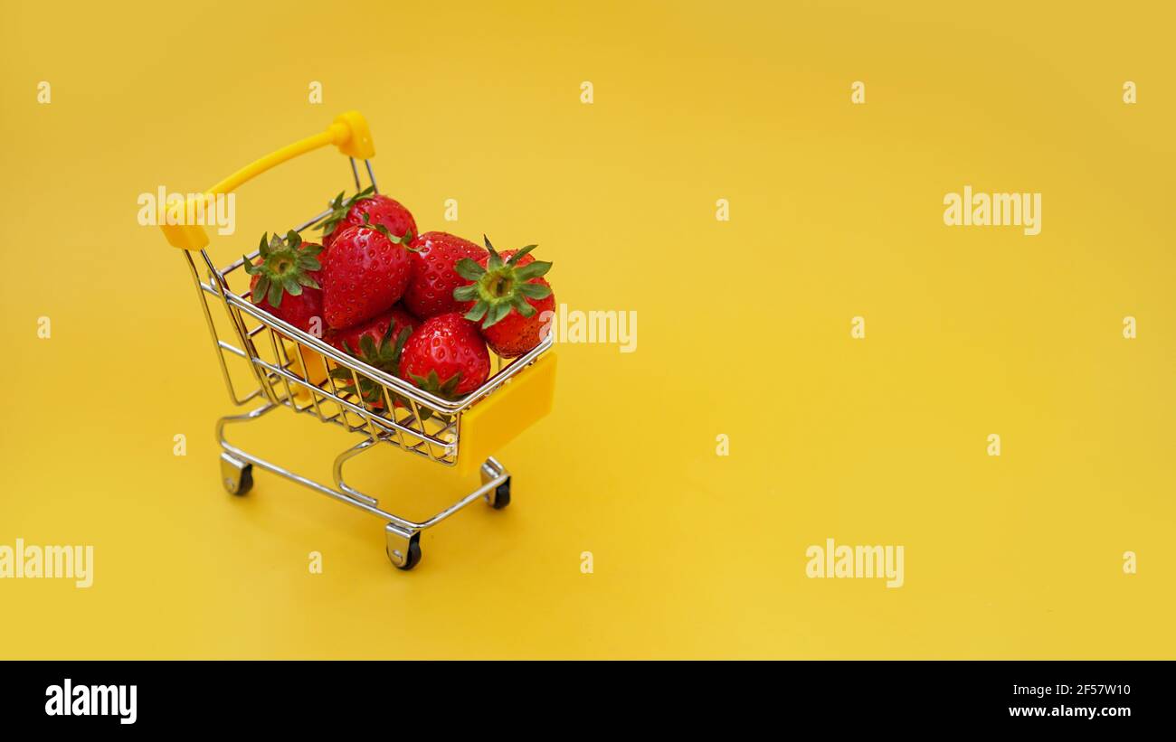 Fragole fresche in un carrello su un giallo brillante sfondo Foto Stock