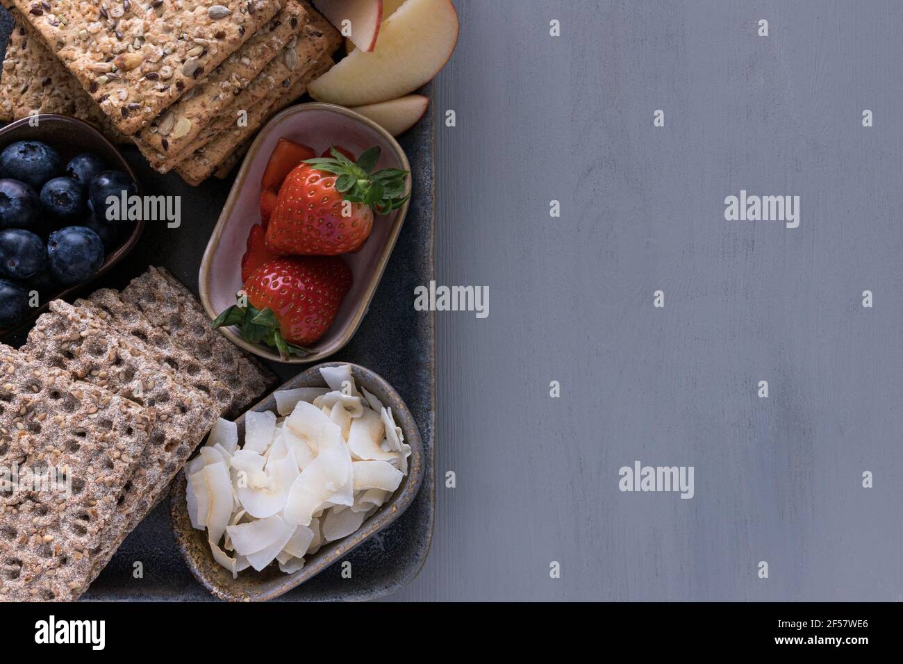 Due pile di cracker croccanti accanto a tre vassoi pieni di frutta sana: Fragole, mirtilli e cocco, su un grande ed elegante vassoio Foto Stock