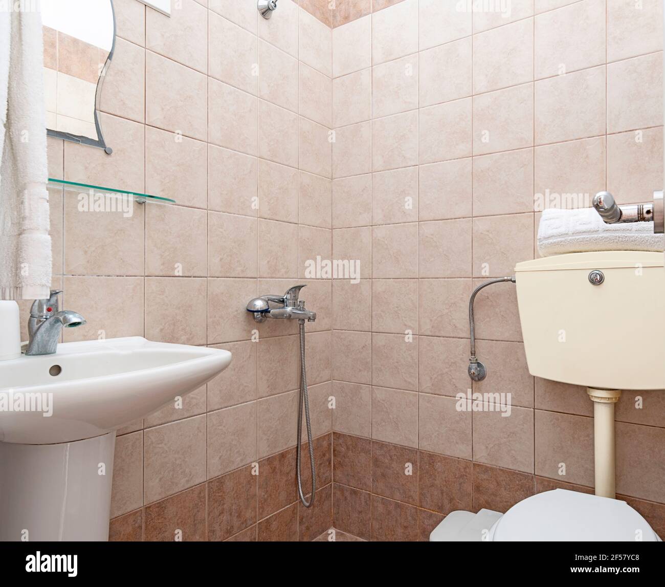 Guardaroba di stile semplice interno di piccolo bagno con pareti in piastrelle di ceramica beige, lavabo bianco, wc classico Foto Stock