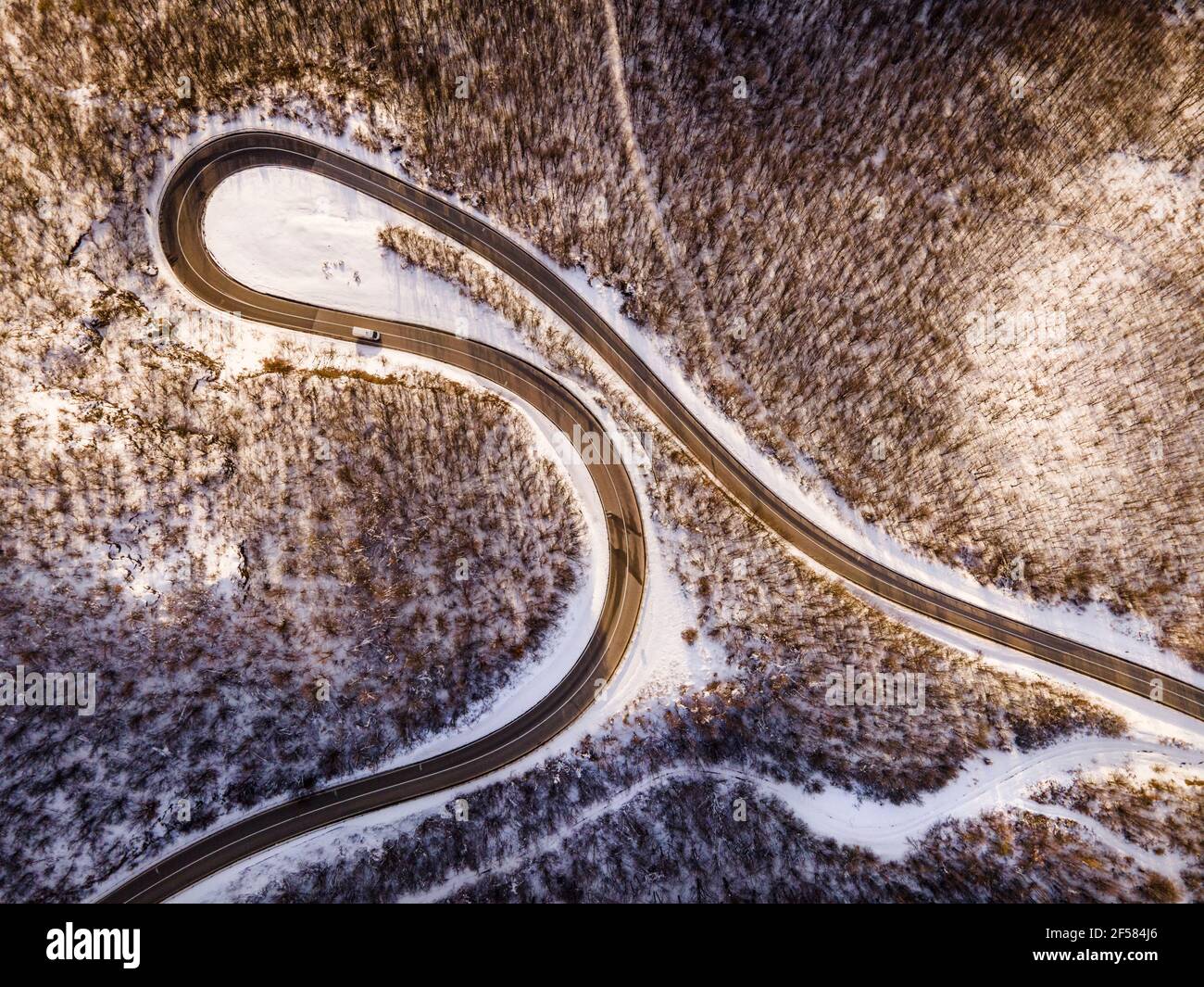 Vista aerea ad angolo alto immagine drone sulla serpentina curva strada attraverso gli alberi e la foresta in catena montuosa con Neve bianca nella giornata invernale vicino a Knja Foto Stock