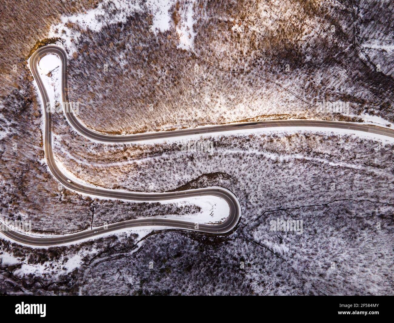 Vista aerea ad angolo alto immagine drone sulla serpentina curva strada attraverso gli alberi e la foresta in catena montuosa con Neve bianca nella giornata invernale vicino a Knja Foto Stock