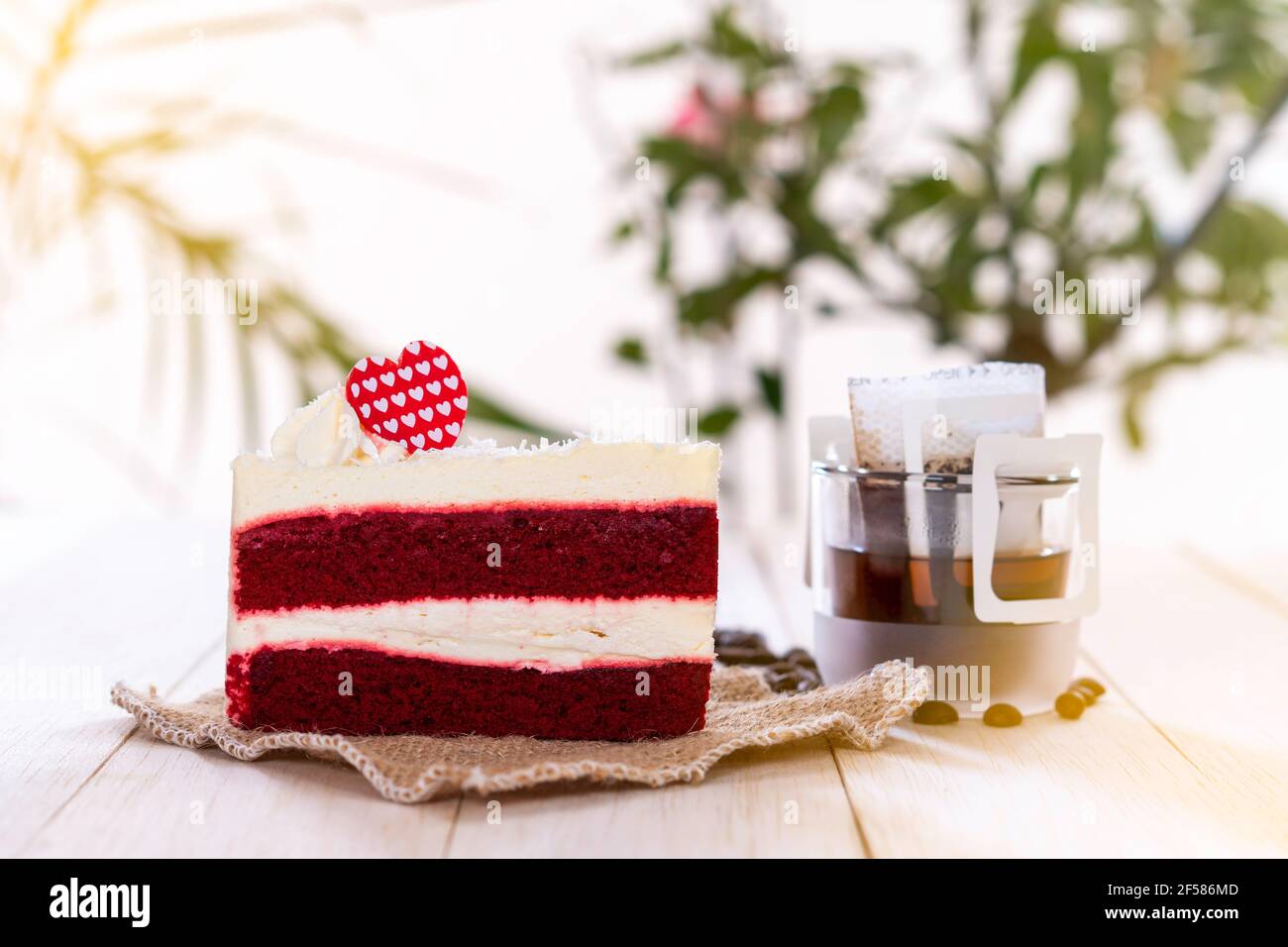 Fetta di torta di velluto rosso e caffè nero caldo gocciola sul tavolo di legno sul giardino. Foto Stock
