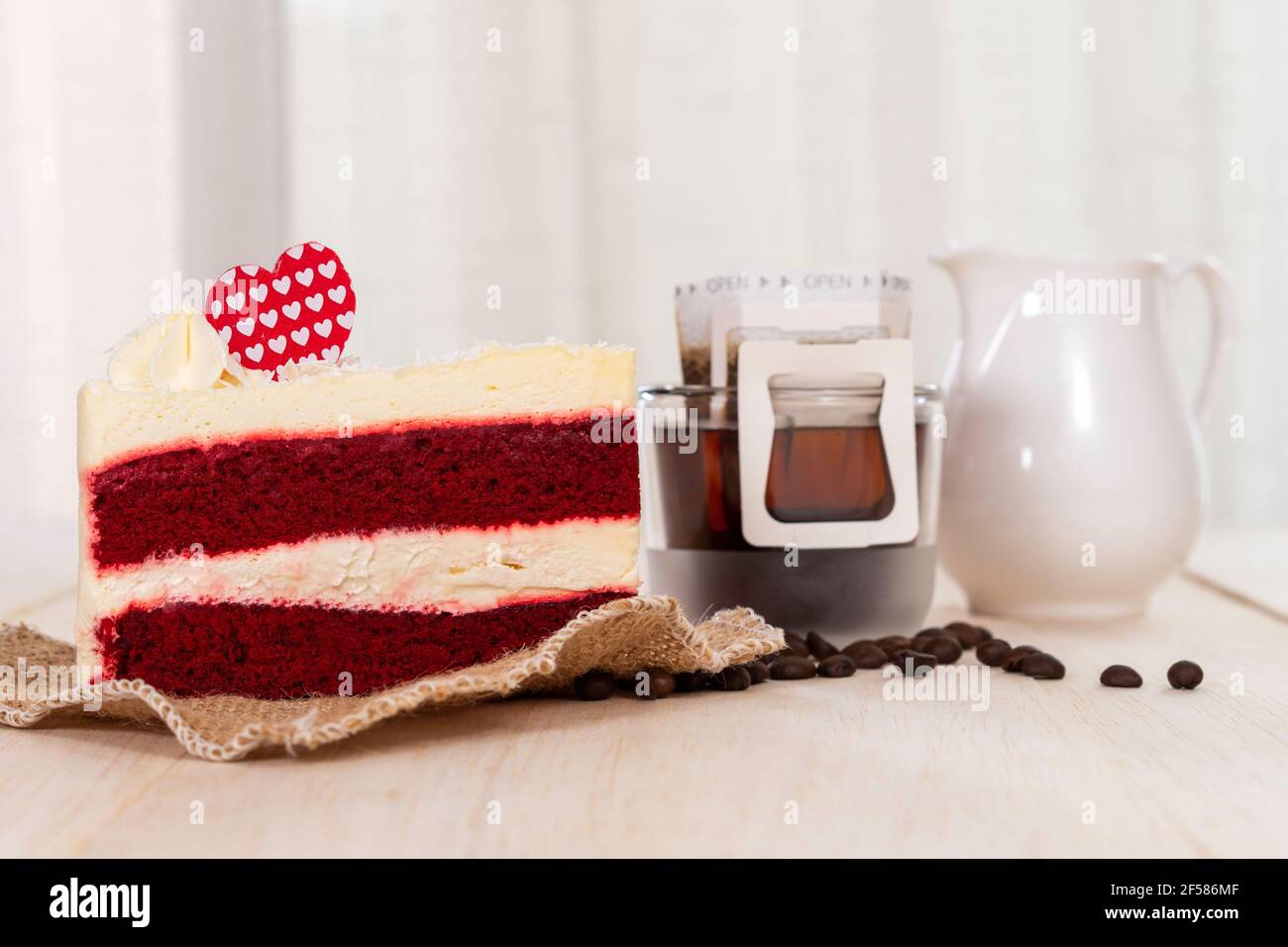 Fetta di torta di velluto rosso e goccia di caffè nero caldo sul tavolo di legno con sfondo bianco tenda. Foto Stock