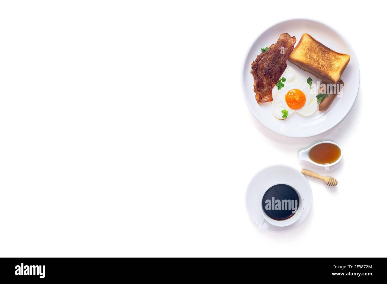 Colazione, pane tostato al burro fresco, uova fritte a forma di cuore, salsiccia affumicata e pancetta alla griglia servita con caffè nero e miele su sfondo bianco, Top Foto Stock