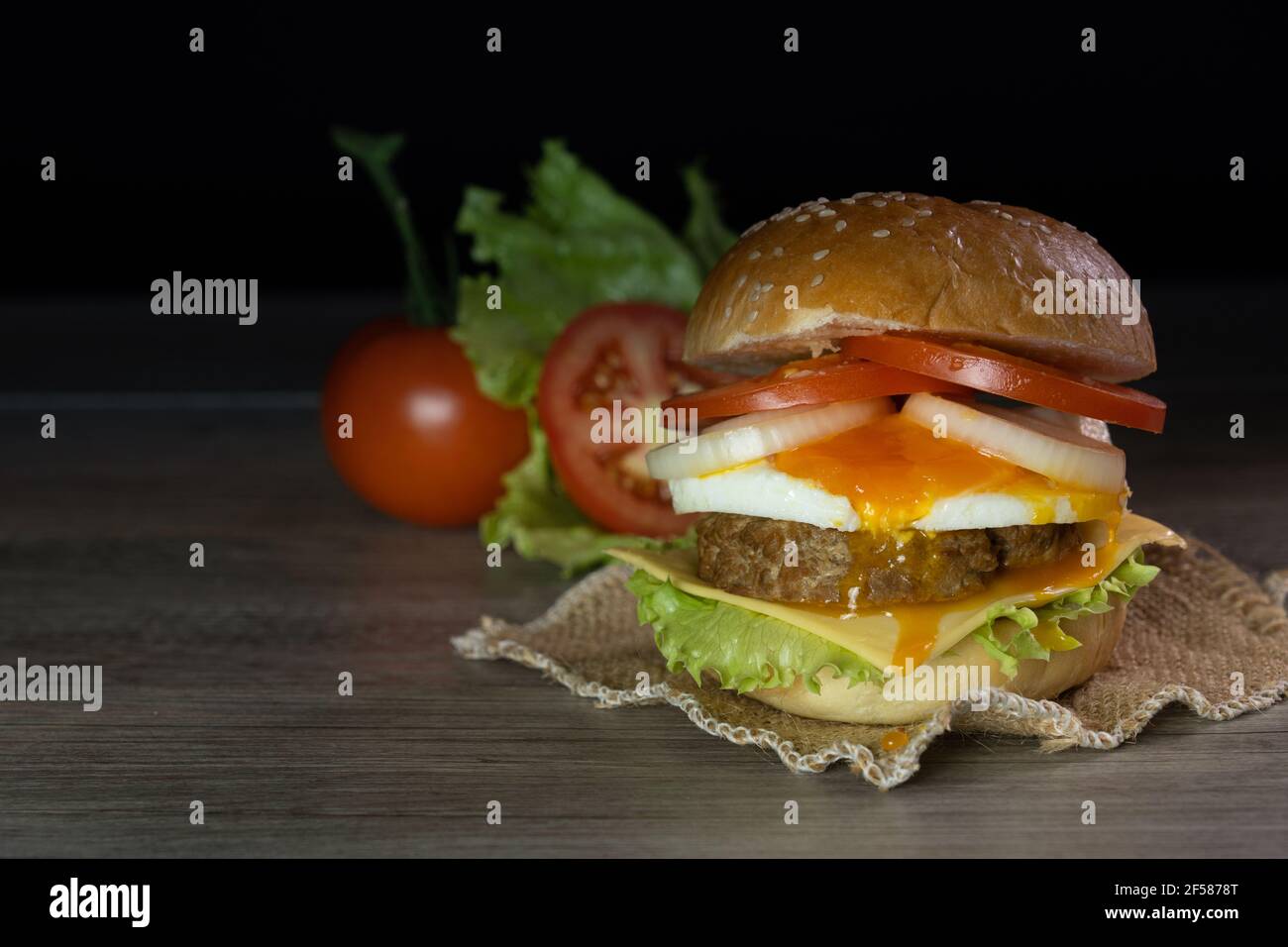 Hamburger, hamburger, cheeseburger, in panna con lattuga, pomodoro, cipolla, uova fritte, deliziosi fast food, su sfondo grigio di legno nero. Foto Stock