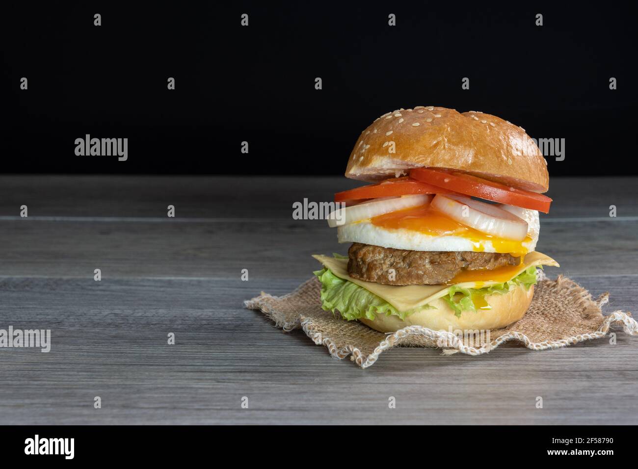 Hamburger, hamburger, cheeseburger, in panna con lattuga, pomodoro, cipolla, uova fritte, deliziosi fast food, su sfondo grigio di legno nero. Foto Stock