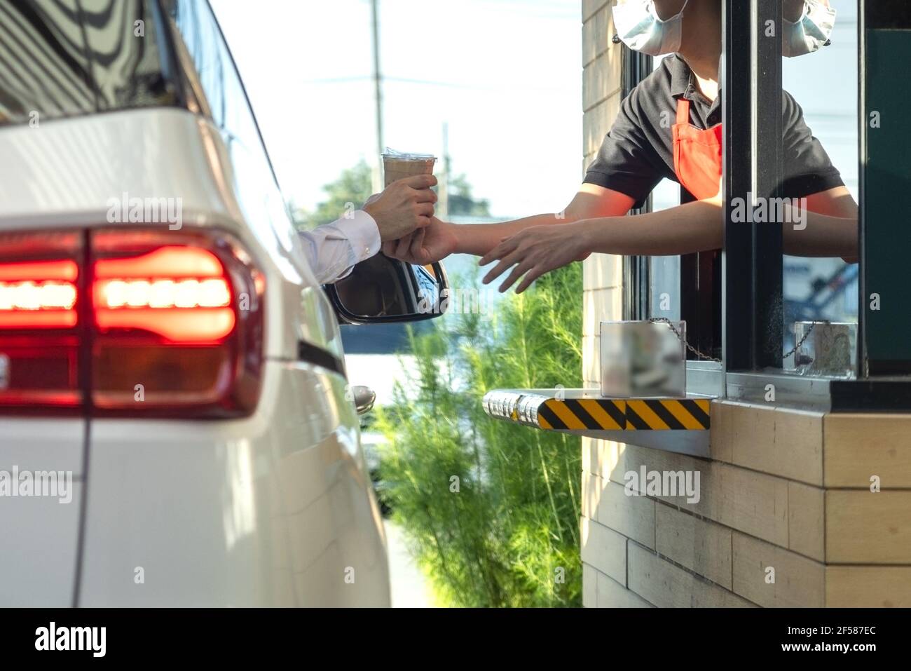 La mano dei clienti nell'automobile sta raccogliendo una tazza personale di caffè dal commesso guidando attraverso (azionamento attraverso). Foto Stock