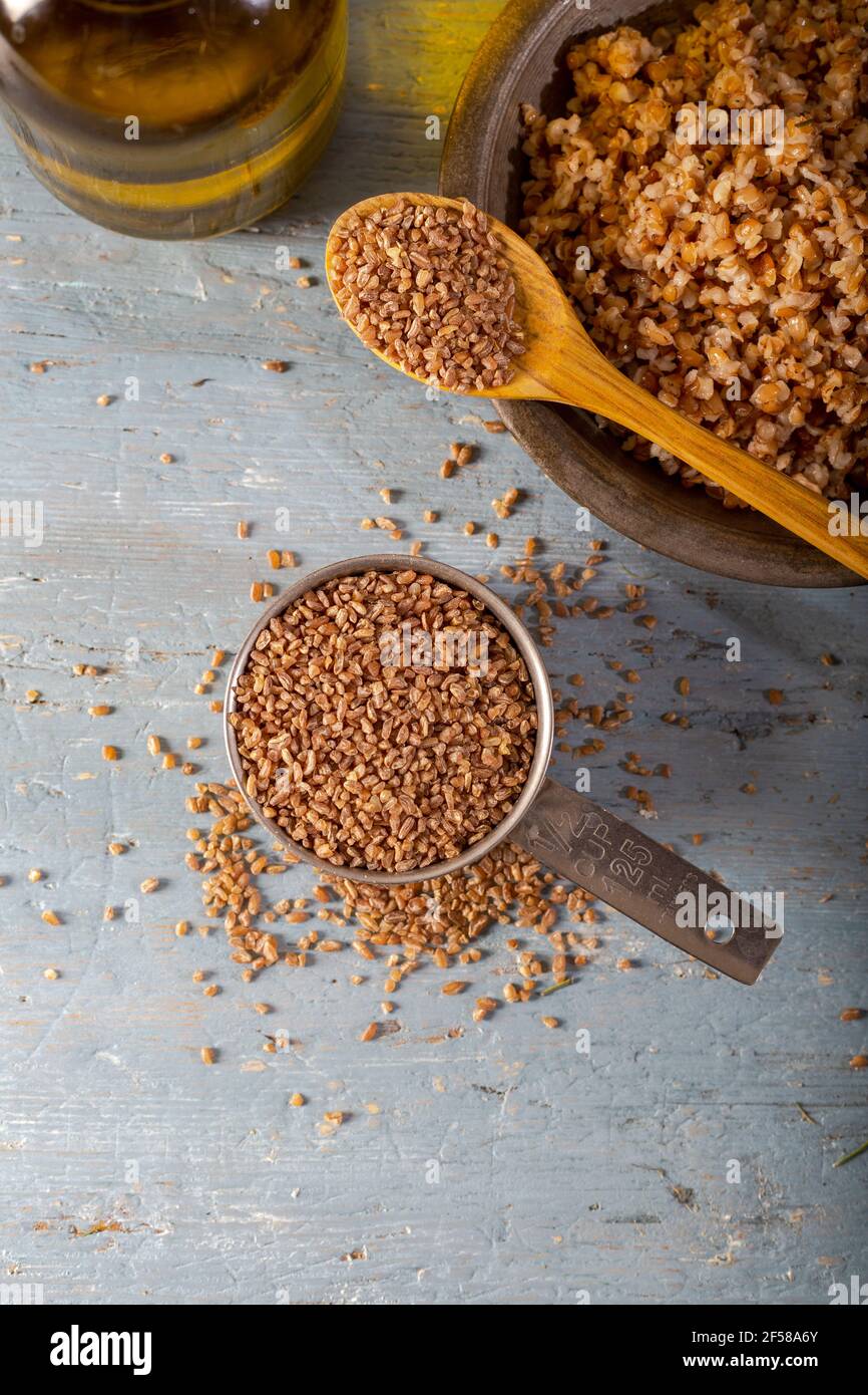 Bulgur Siyez in recipiente di misurazione in metallo su tavolo di legno blu. (Einkorn bulgur) Foto Stock