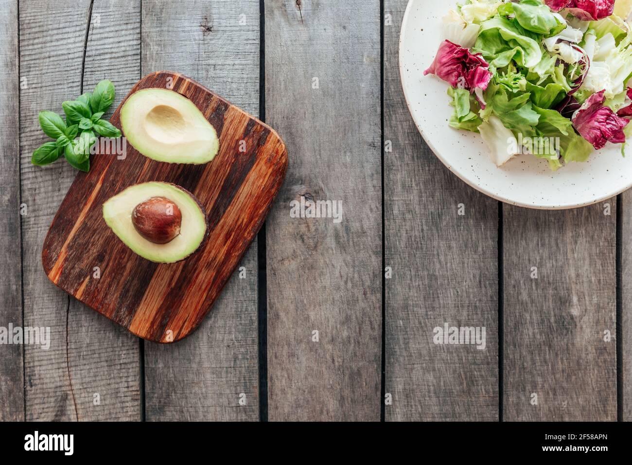 Concetto sano di mangiare piatto posato. Dieta mediterranea, piatto con foglie fresche di insalata di lattuga verde, foglie di radicchio viola, tagliere con avocado Foto Stock