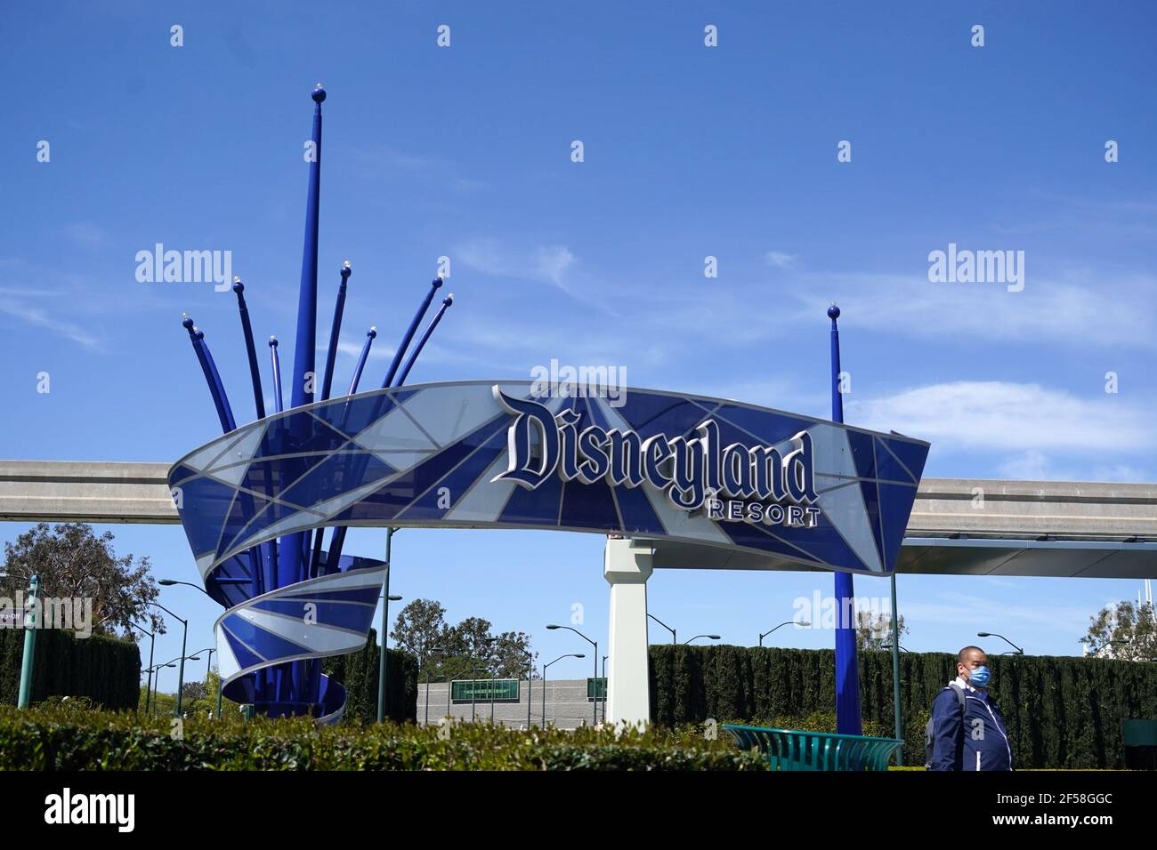 Un uomo con una maschera si trova di fronte al cartello Disneyland Resort, mercoledì 24 marzo 2021, ad Anaheim, Calif. Foto Stock