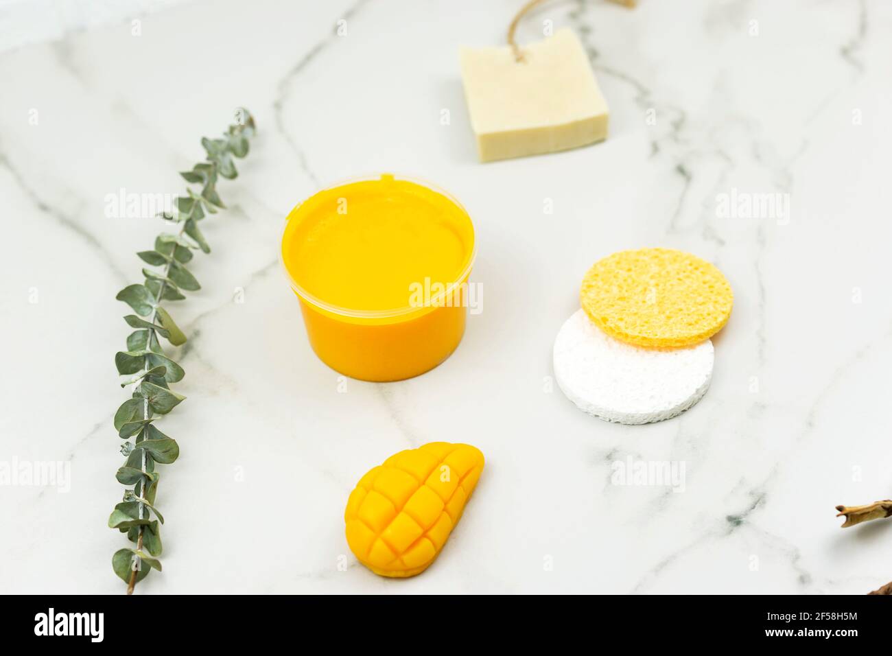 Un mango giallo fatto a mano sapone, un ramo di eucalipto, una spazzola per il massaggio, olio giacciono su un tavolo bianco. Concetto positivo per il corpo Foto Stock