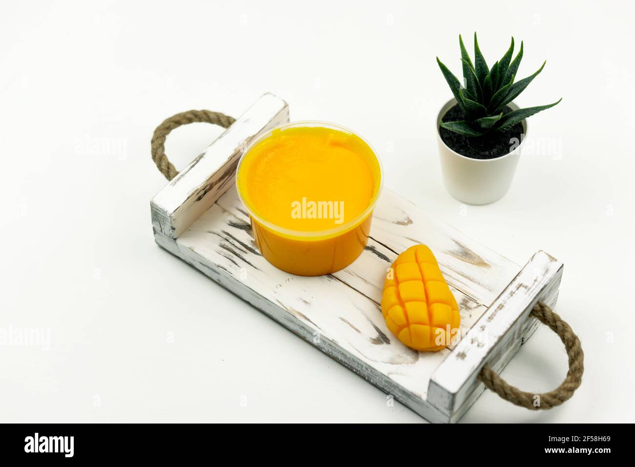 Una mano gialla di mango ha fatto sapone e uno scrub di mango per la cura del corpo, posizionarsi sul vassoio di legno bianco in il bagno moderno Foto Stock