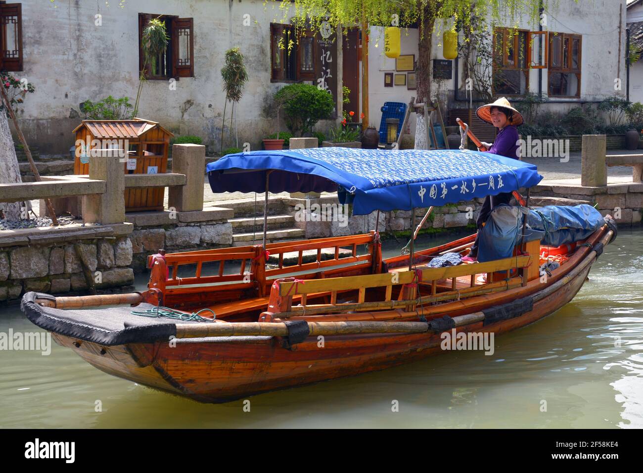 Una signora naviga la sua barca turistica attraverso il canale della più votata zona panoramica cinese di Zhouzhuang nella provincia di Jiangsu. Foto Stock
