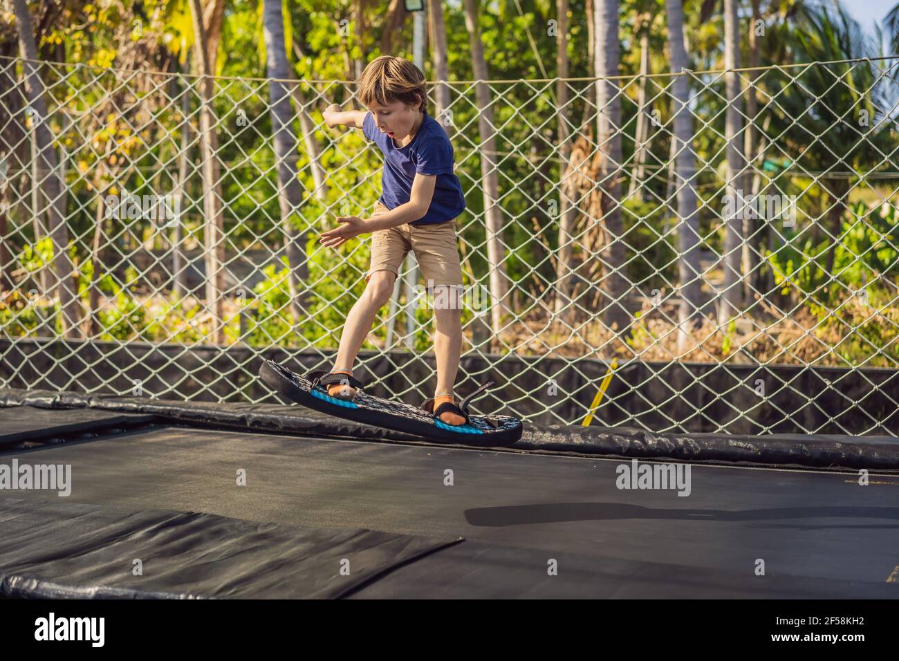 Happy boy su una tavola morbida per un trampolino che salta su un trampolino  all'aperto, sullo sfondo di palme. Il trampolino è come un Foto stock -  Alamy