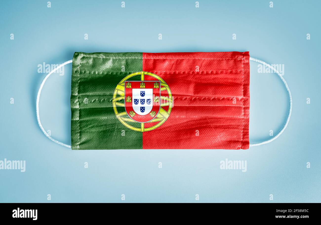 Covid-19 concetto di protezione Coronavirus: Maschera medica monouso con bandiera portoghese su sfondo blu. CHI raccomanda l'uso della maschera per la sicurezza. Foto Stock