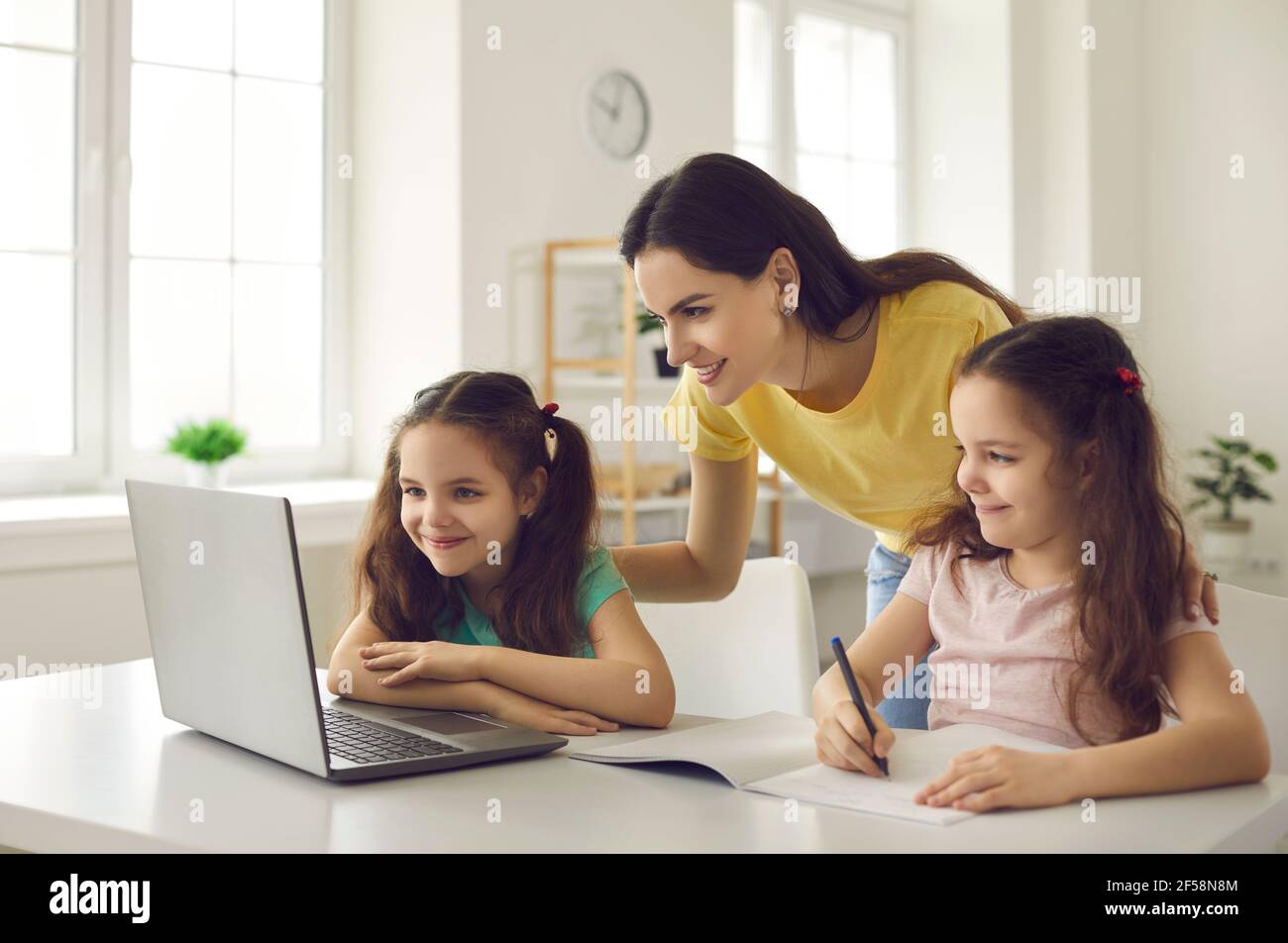 La madre premurosa aiuta i suoi figli a imparare usando un computer portatile per studiare le lezioni scolastiche. Foto Stock