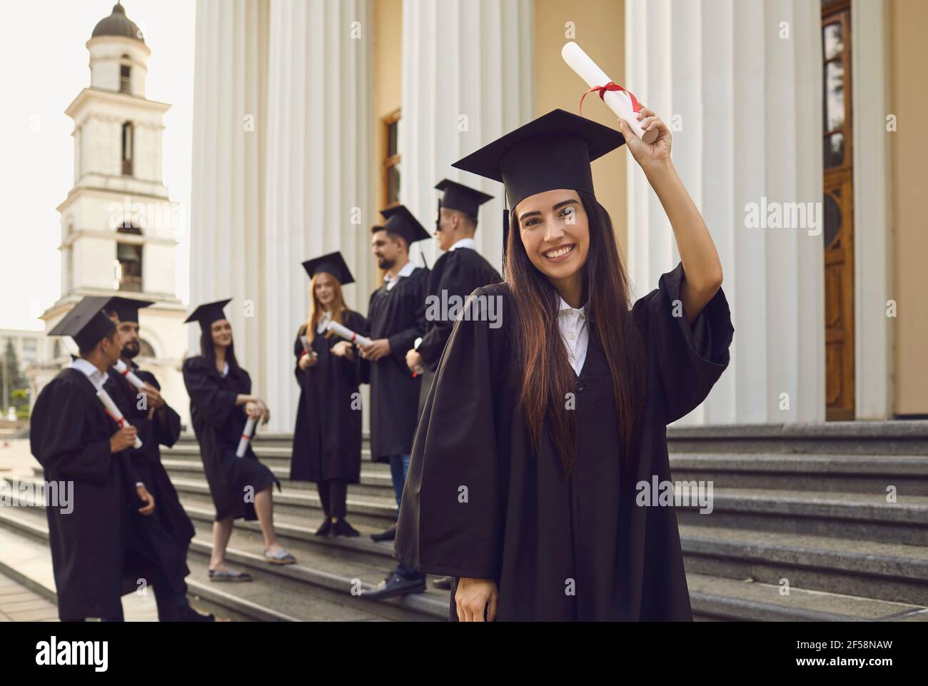 Allievo allegro in abito graduato e con rotolo di diploma Foto Stock