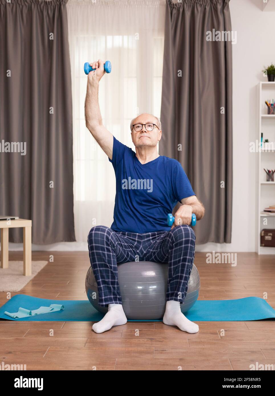 Uomo anziano che fa sport con i pesi. Anziano pensionato online internet esercizio di formazione a casa attività sportiva con manubri, banda di resistenza, palla svizzera all'età di anziano pensionamento. Foto Stock