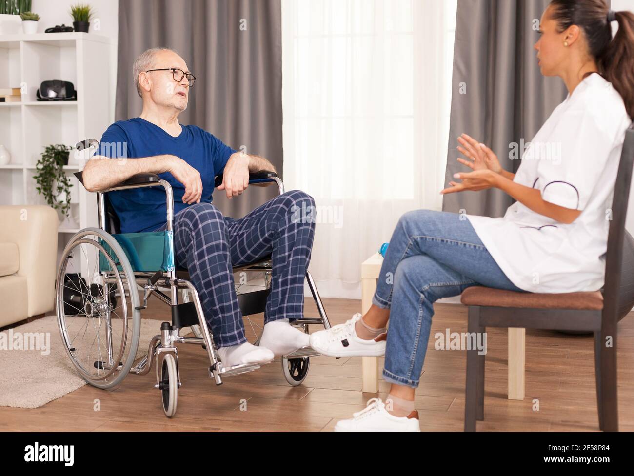 Lavoratore medico che spiega il trattamento all'uomo anziano in sedia a rotelle. Invalidità persona anziano con operatore medico in assistenza infermieristica a casa, assistenza sanitaria e medicina Foto Stock