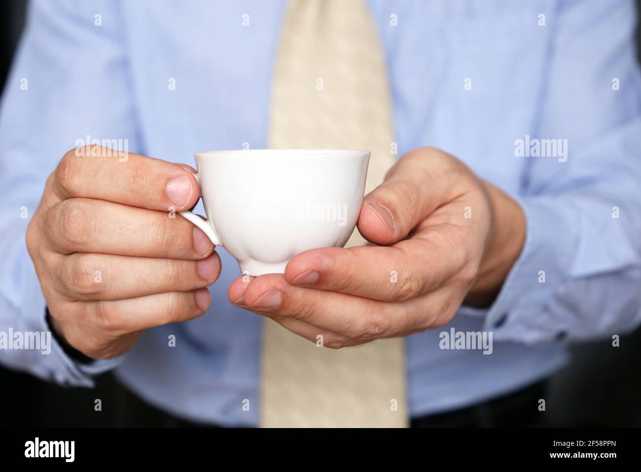 Uomo in ufficio vestiti con caffè. Tazza bianca di bevanda calda in mani maschili, pausa durante il lavoro in ufficio Foto Stock