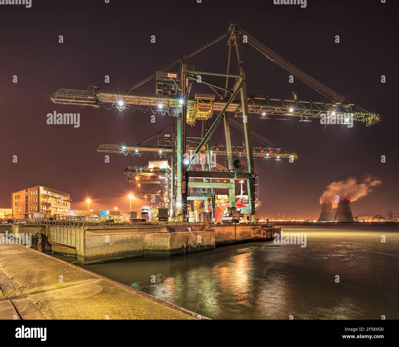 Scena notturna con gru massiccia sul terminal dei container illuminato, Porto di Anversa, Belgio. Foto Stock