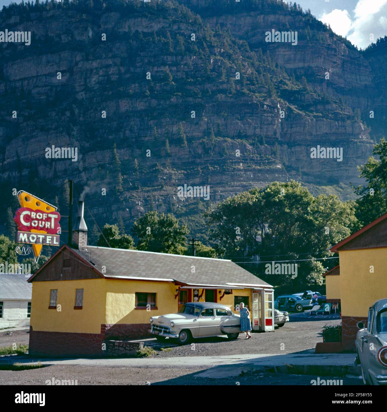 Il check-in/ufficio presso il Croft Court Motel, nella città di Ouray, Ouray County, Colorado, USA c. 1960. Il colorato e modernista cartello al neon contrasta con il suggestivo ambiente naturale delle montagne alle spalle. Il clima e lo scenario alpino di Ouray gli valse il soprannome, la ‘Sstrega d’America’. Originariamente fondata dai minatori in cerca di argento e oro nelle montagne circostanti, i prospettori sono arrivati nella zona nel 1875. Questa immagine proviene da una vecchia trasparenza amatoriale dei colori americani – una fotografia d'epoca degli anni '50/60. Foto Stock