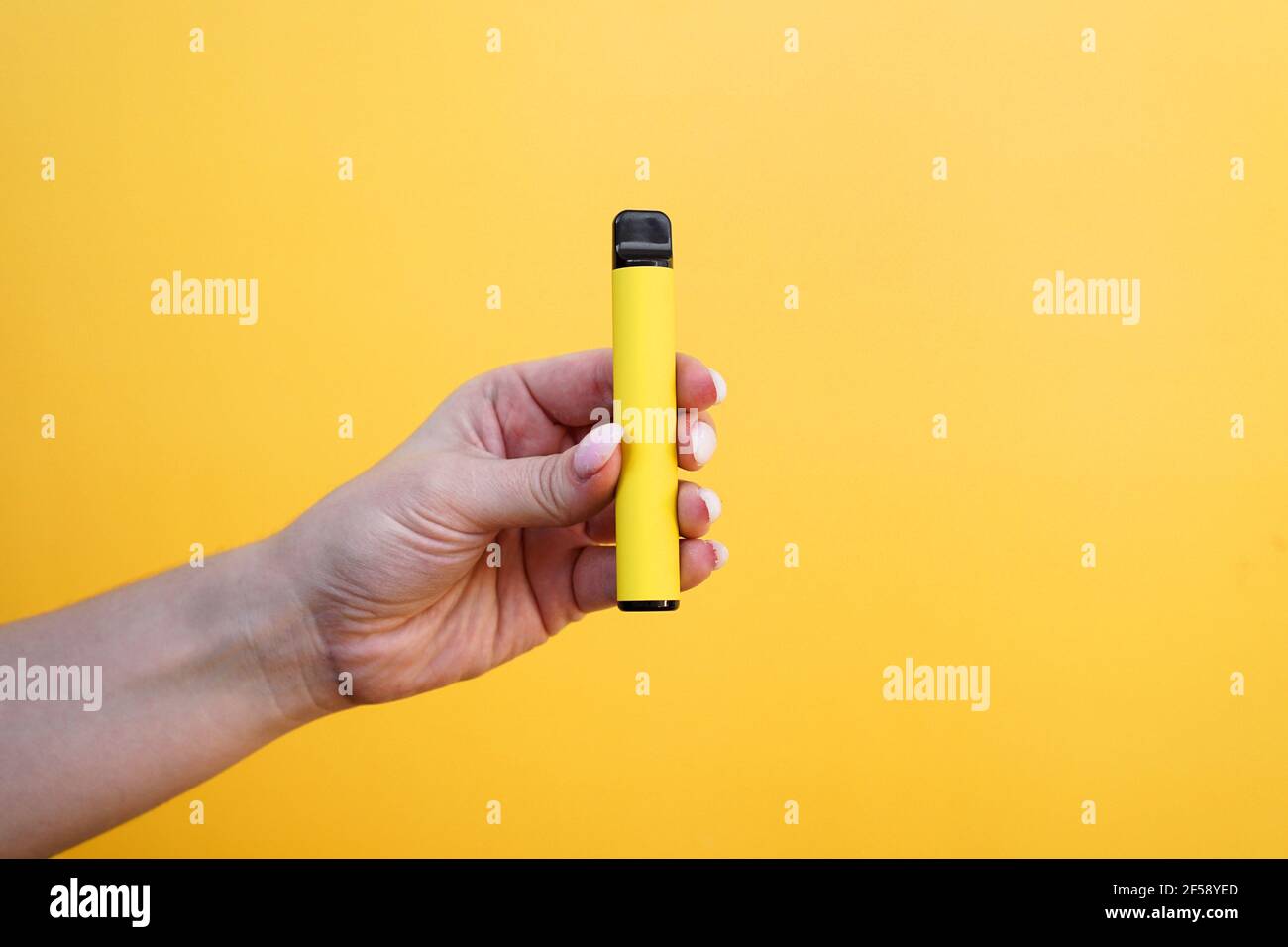 Sigaretta elettronica monouso gialla in mano femminile. Sfondo giallo brillante Foto Stock