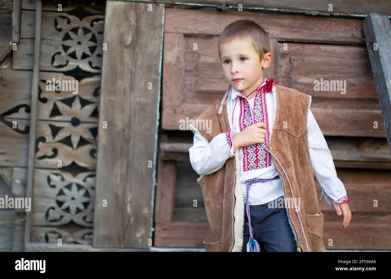 Ragazzino in abiti nazionali slavi su sfondo di legno. Bambino bielorusso o ucraino in una camicia ricamata. Foto Stock