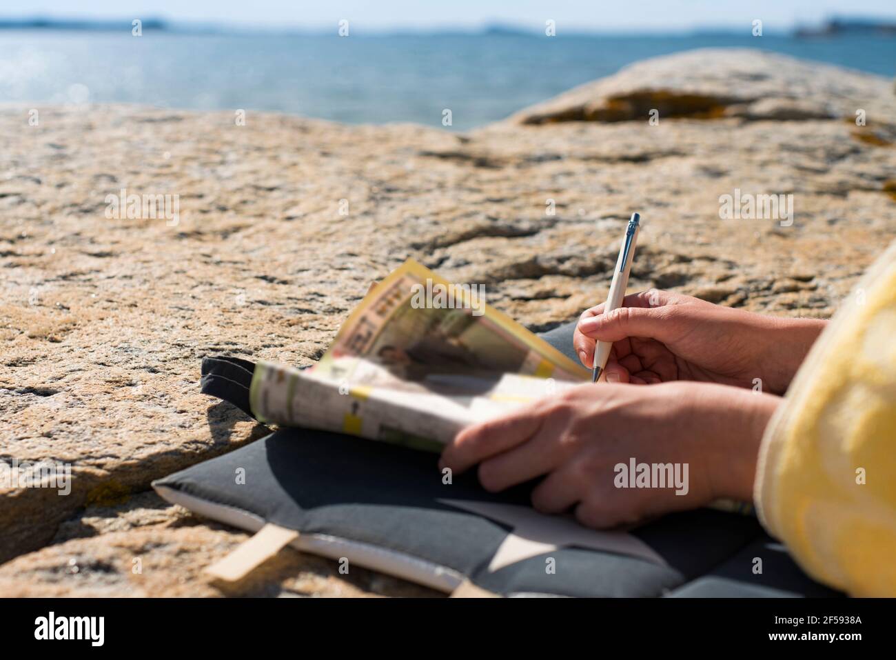 Donna che si rilassa sulla spiaggia risolvendo Crosswords durante la giornata estiva di vacanza. Foto Stock