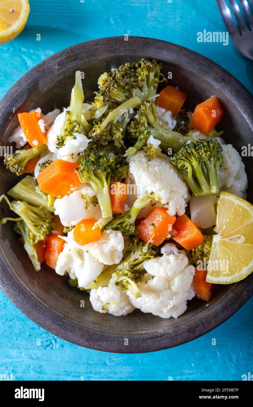 Broccoli, cavolfiore e insalata di carote in ciotola su tavolo di legno blu con olio d'oliva e fette di limone. Vista dall'alto. Primo piano. Foto Stock