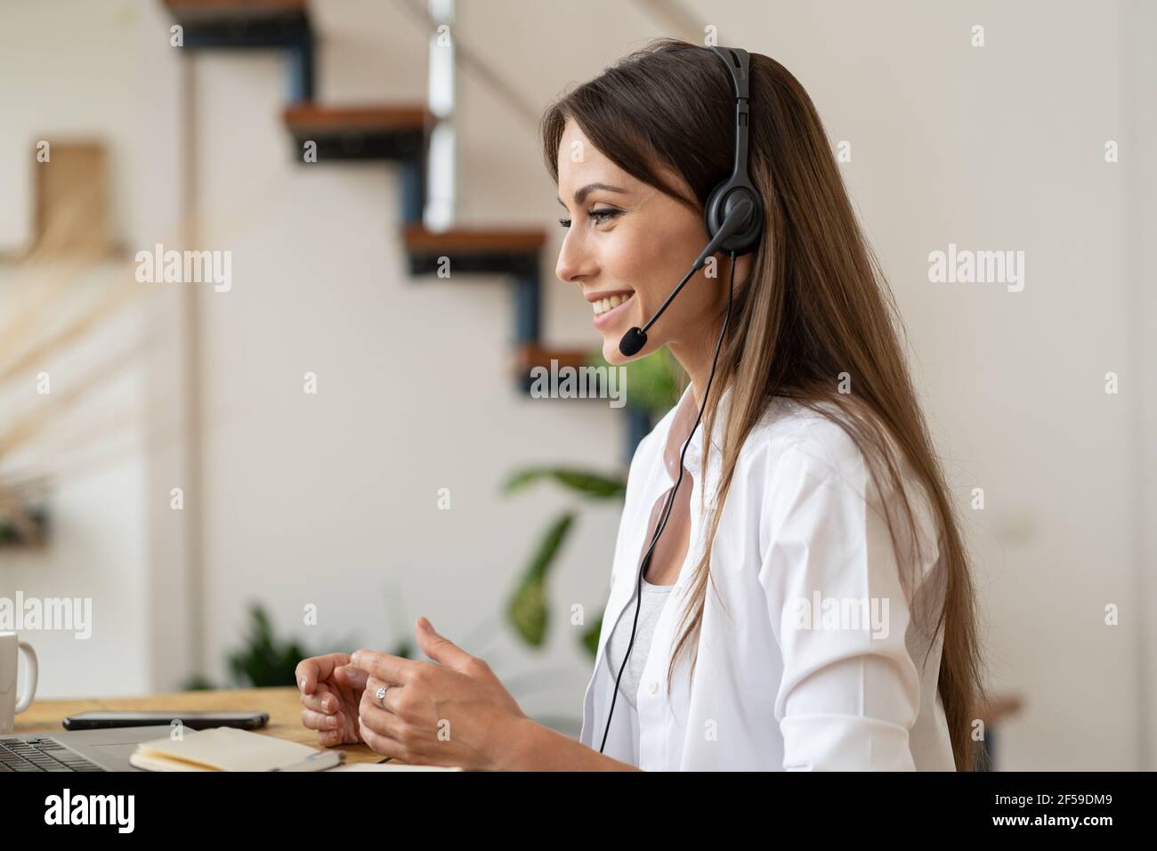 Ragazza dipendente con cuffie che guarda il computer portatile e parla in videochiamata lavorando da casa. Foto Stock