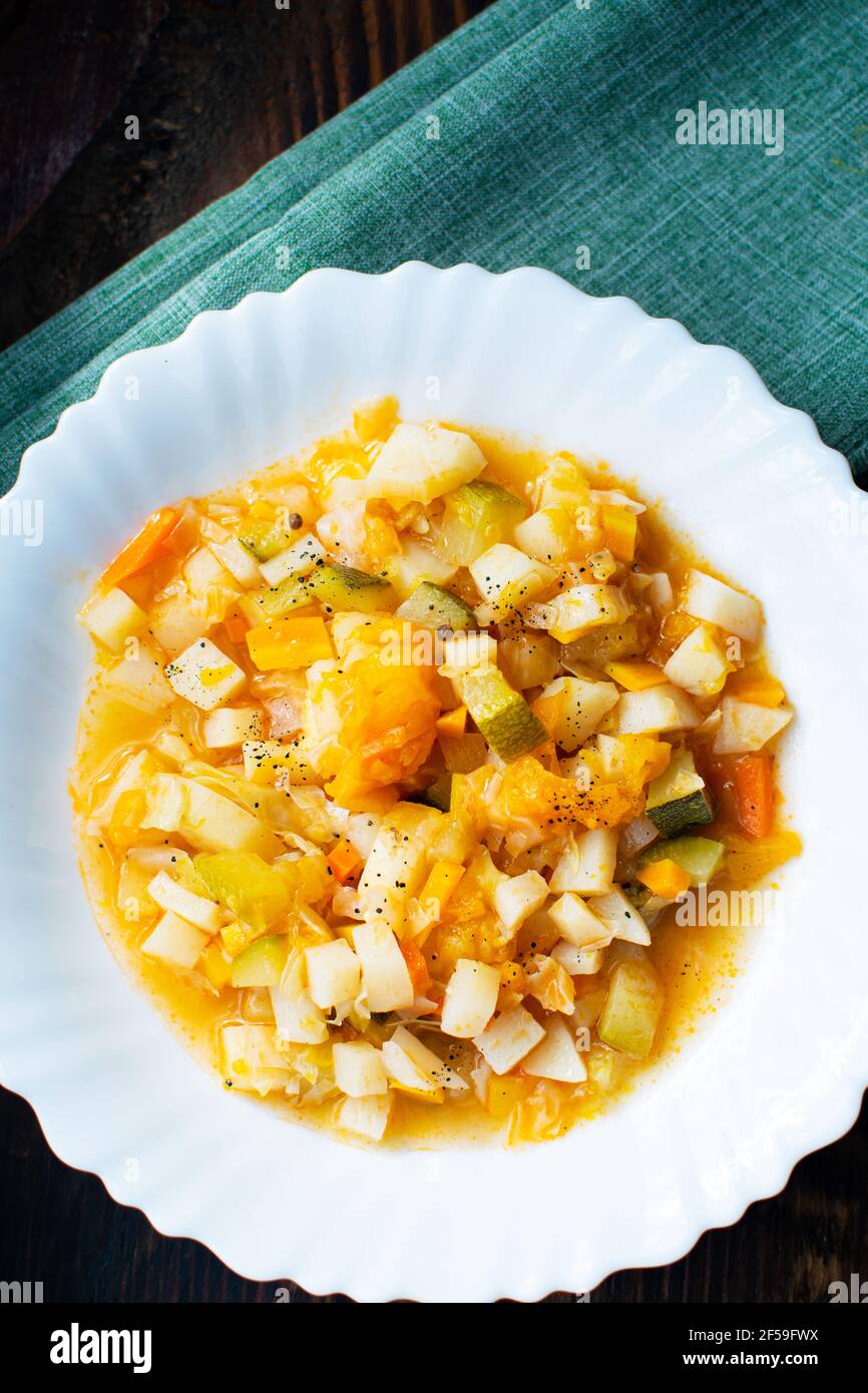 Mescolate le verdure stufate su un piatto bianco al caffè. Stufato di verdure in salsa di pomodoro. Cibo vegetariano o vegano cucinato. Foto Stock