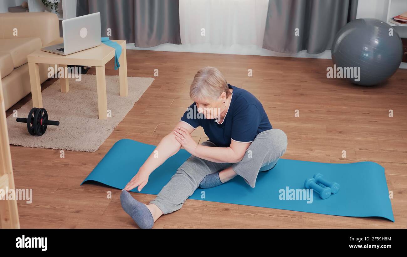 Donna anziana attiva che stende il corpo sul tappetino yoga. Anziano pensionati allenano a casa attività sportive in età pensionabile anziana Foto Stock