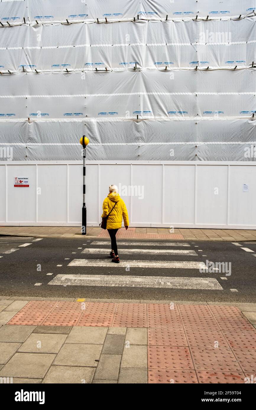 Londra UK, marzo 25 2021, una donna che indossa un camice giallo brillante che attraversa UNA strada a un pedone o Zebra Crossing Foto Stock