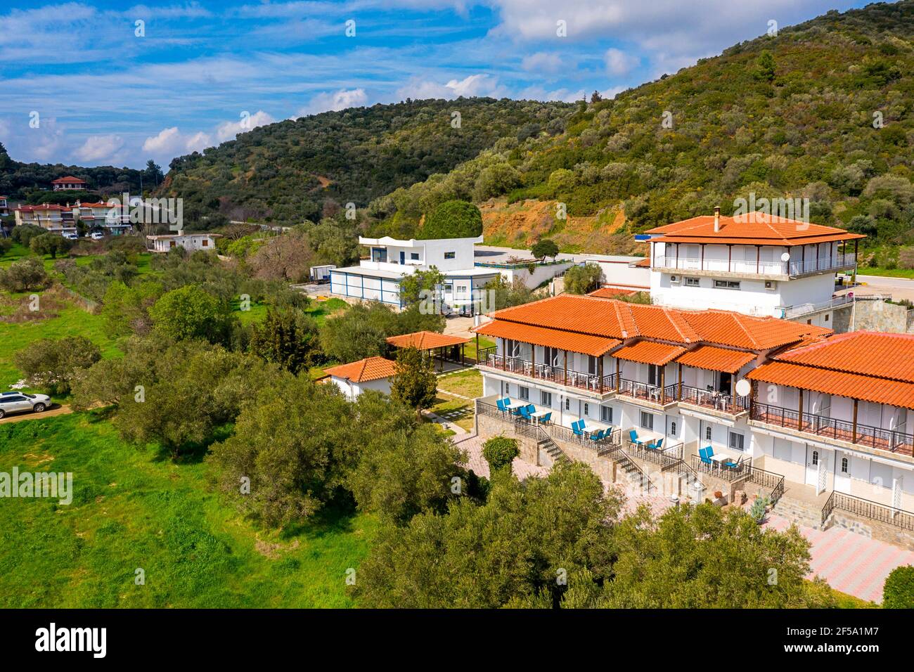 Drone aereo vista dall'alto campagna paesaggio estivo con bianche case residenziali tra verdi colline di ulivi, cielo blu sfondo ambiente Foto Stock