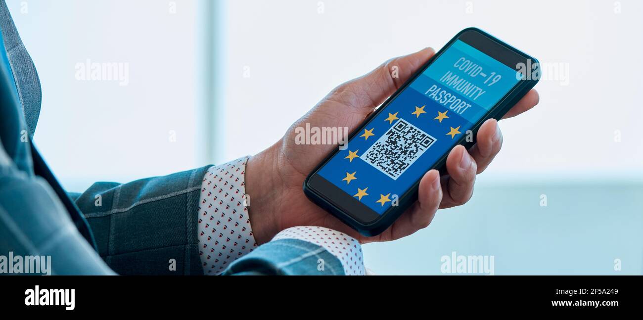 l'uomo d'affari, nella sala d'attesa di un aeroporto, ha un passaporto elettronico simulato europeo covid-19 immunità nello schermo del suo smartphone, in un p Foto Stock
