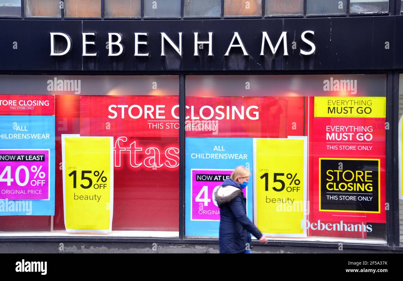 Una donna passa davanti a una finestra di un negozio Debenhams a Manchester, Greater Manchester, Inghilterra, Regno Unito, che mostra poster di "chiusura di punti vendita" Foto Stock