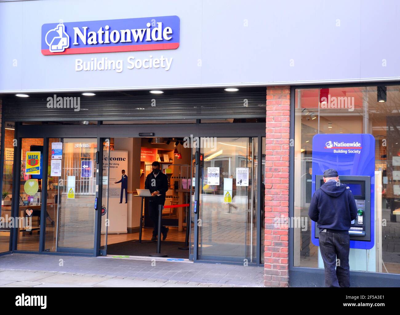 Esterno della filiale della Nationwide Building Society in Market Street, Manchester, Inghilterra, Regno Unito. Uomo a ATM. Dipendente interno per salutare i clienti. Foto Stock