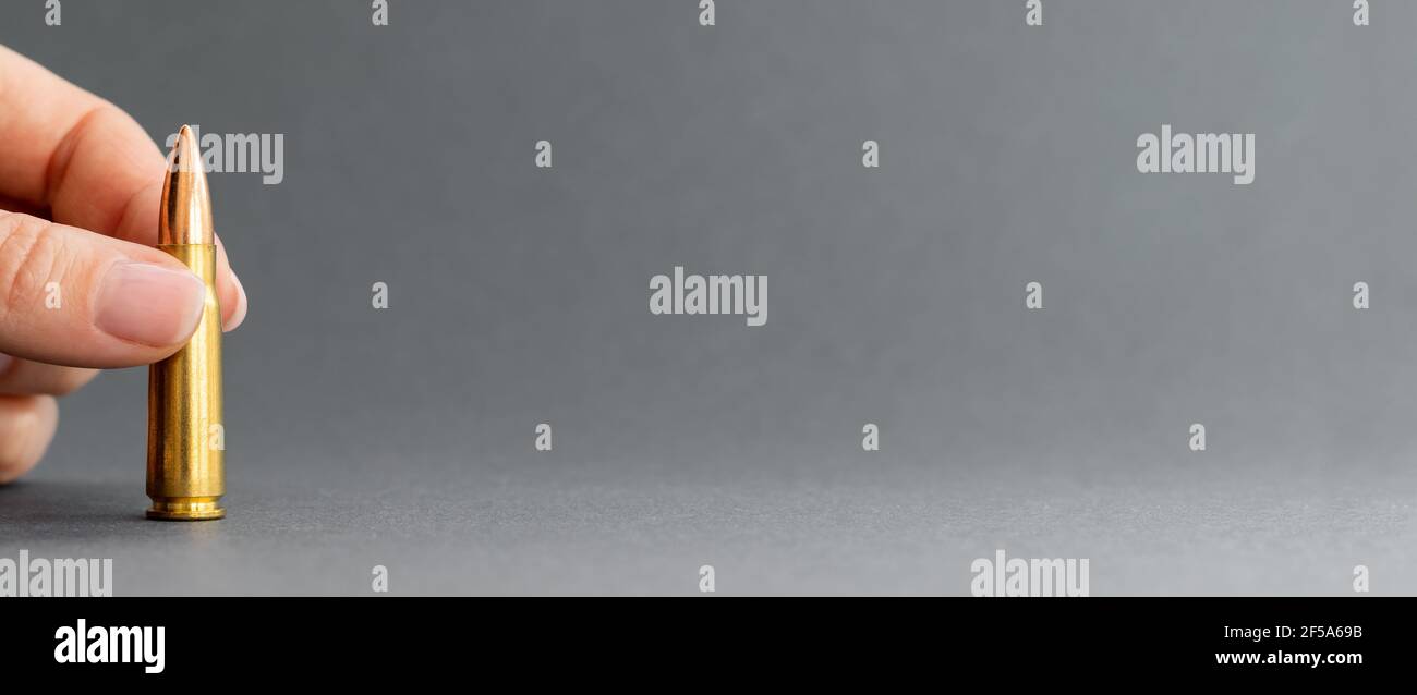 Mano con puntino su sfondo grigio. Cartuccia calibro 7.62 per fucile d'assalto Kalashnikov in dita closeup ampio banner con spazio di copia. Foto Stock