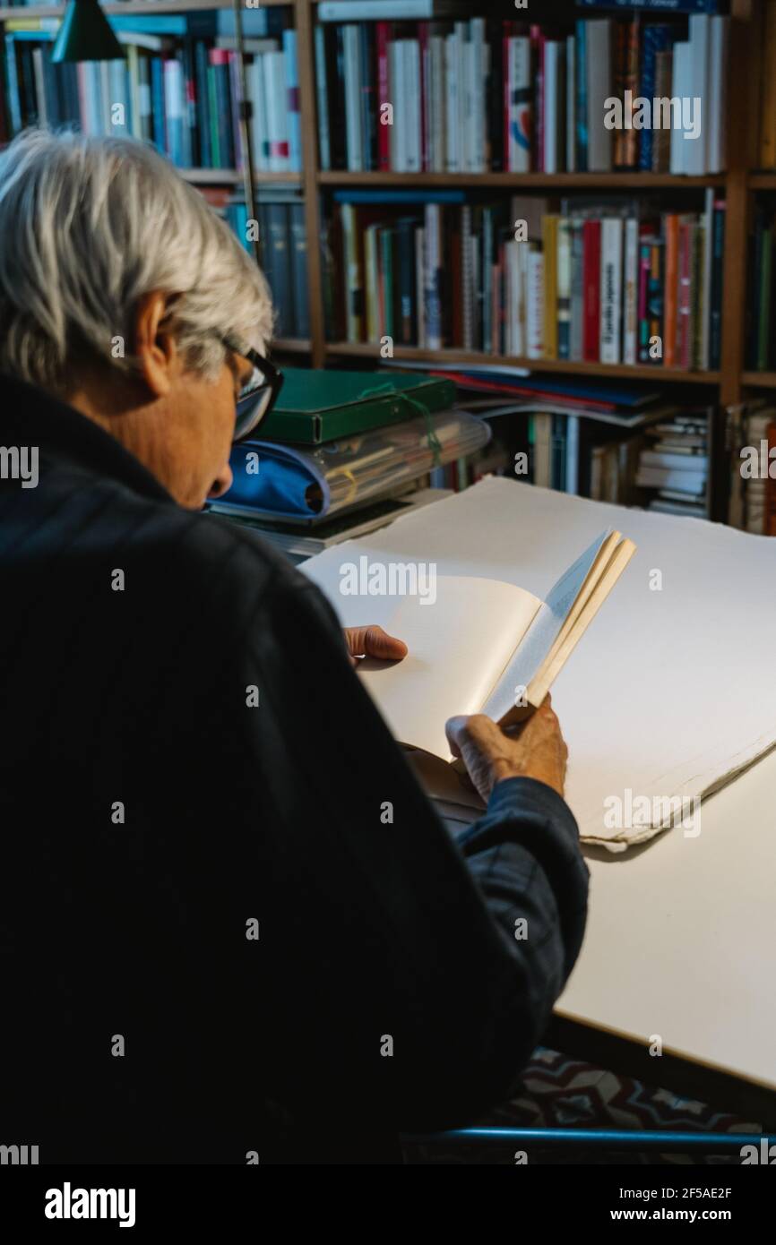 vecchio che legge un libro nella sua biblioteca domestica Foto Stock