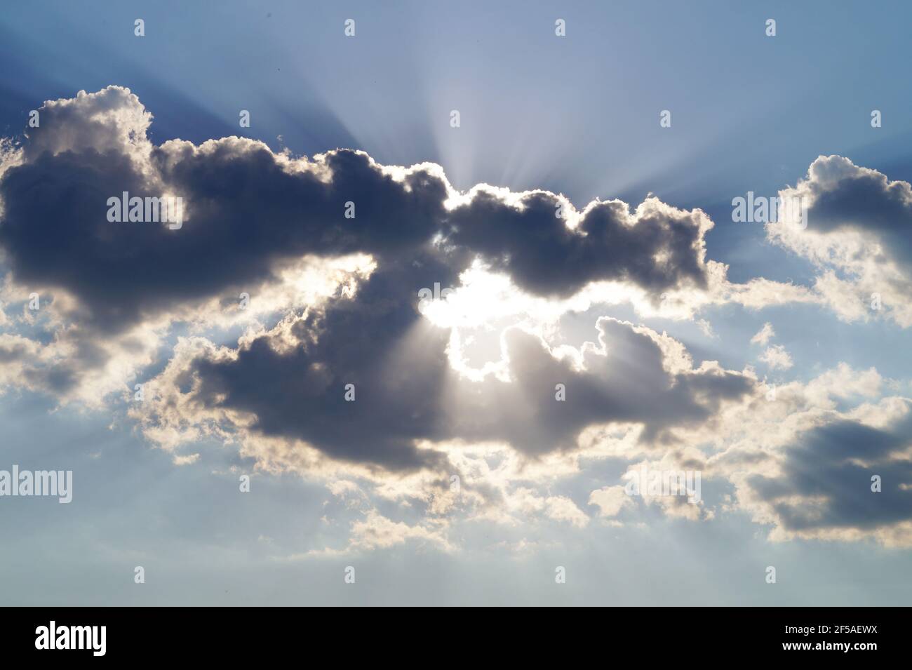 I raggi del sole sbirciano da dietro le nuvole grigie nel cielo Foto Stock