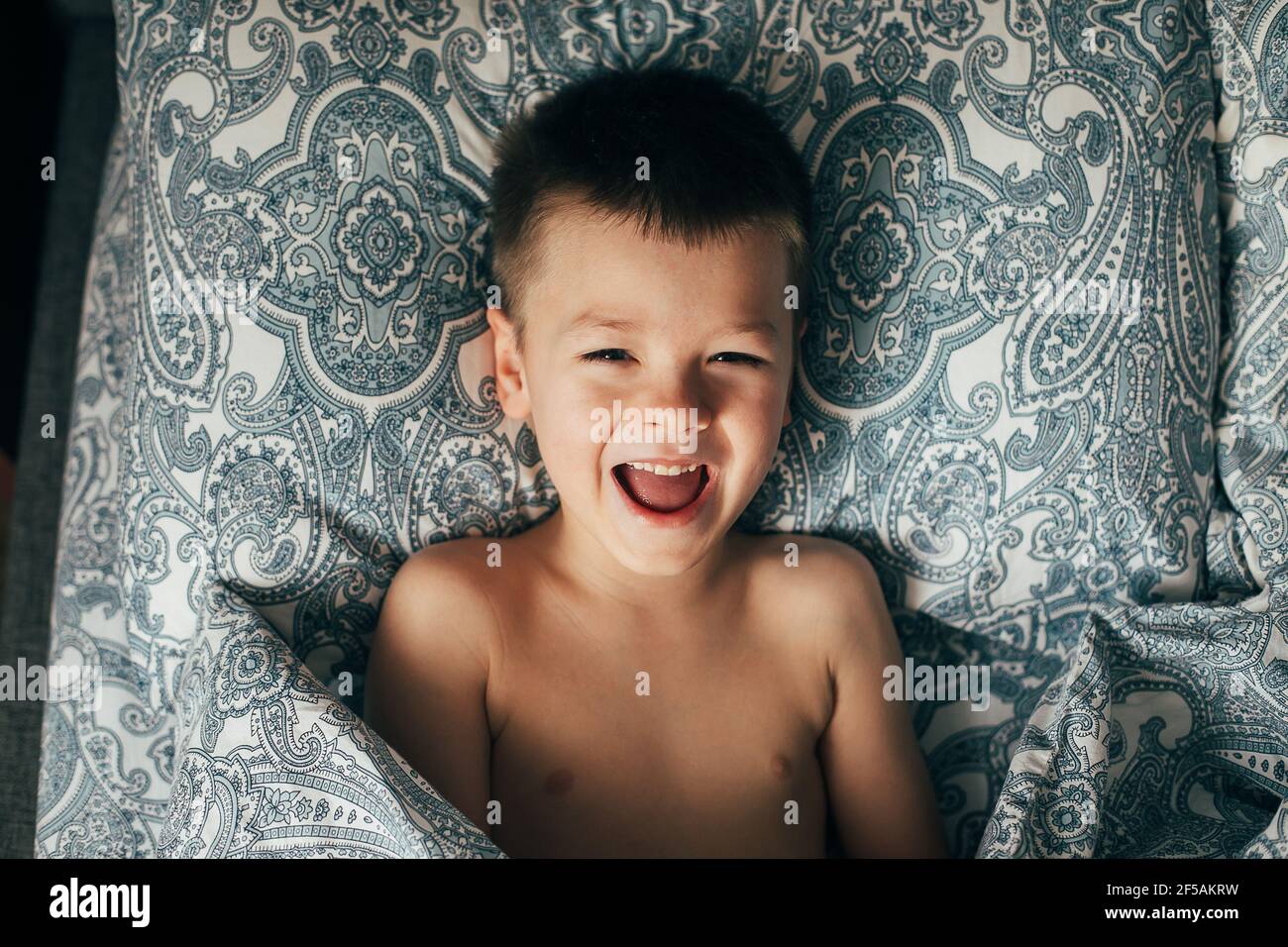 Carino bambino felice ragazzo sorridente, divertendosi a letto a casa. Stile di vita, momento autentico. Foto Stock