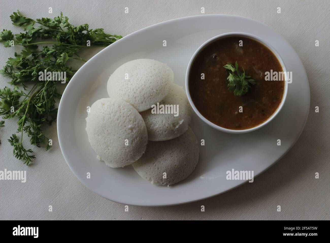 Idli Sambhar un cibo indiano tipicamente fatto in India del Sud ma gradito e preparato quasi in tutte le parti dell'India. Placcato bene. Scatto su sfondo bianco Foto Stock