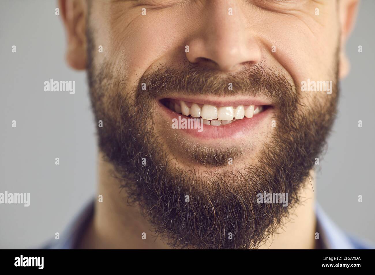 Primo piano studio di foto della parte inferiore del volto di felice giovane sorridente con barba marrone Foto Stock