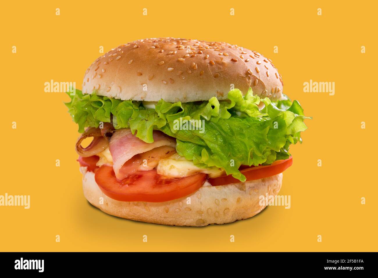 cheeseburger con pancetta, panino ripieno con pancetta, fette di pomodoro, formaggio e insalata di lattuga, isolato su sfondo giallo Foto Stock