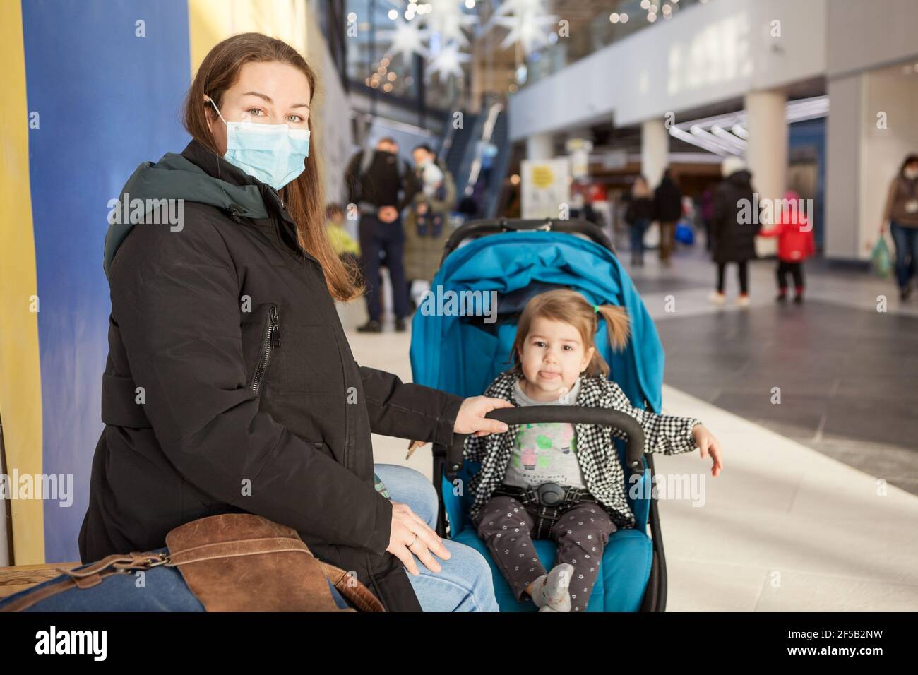 Madre caucasica che riposa con sua figlia seduta in carrozza per bambini, famiglia che cammina in un centro commerciale, donna adulta che indossa la maschera facciale Foto Stock