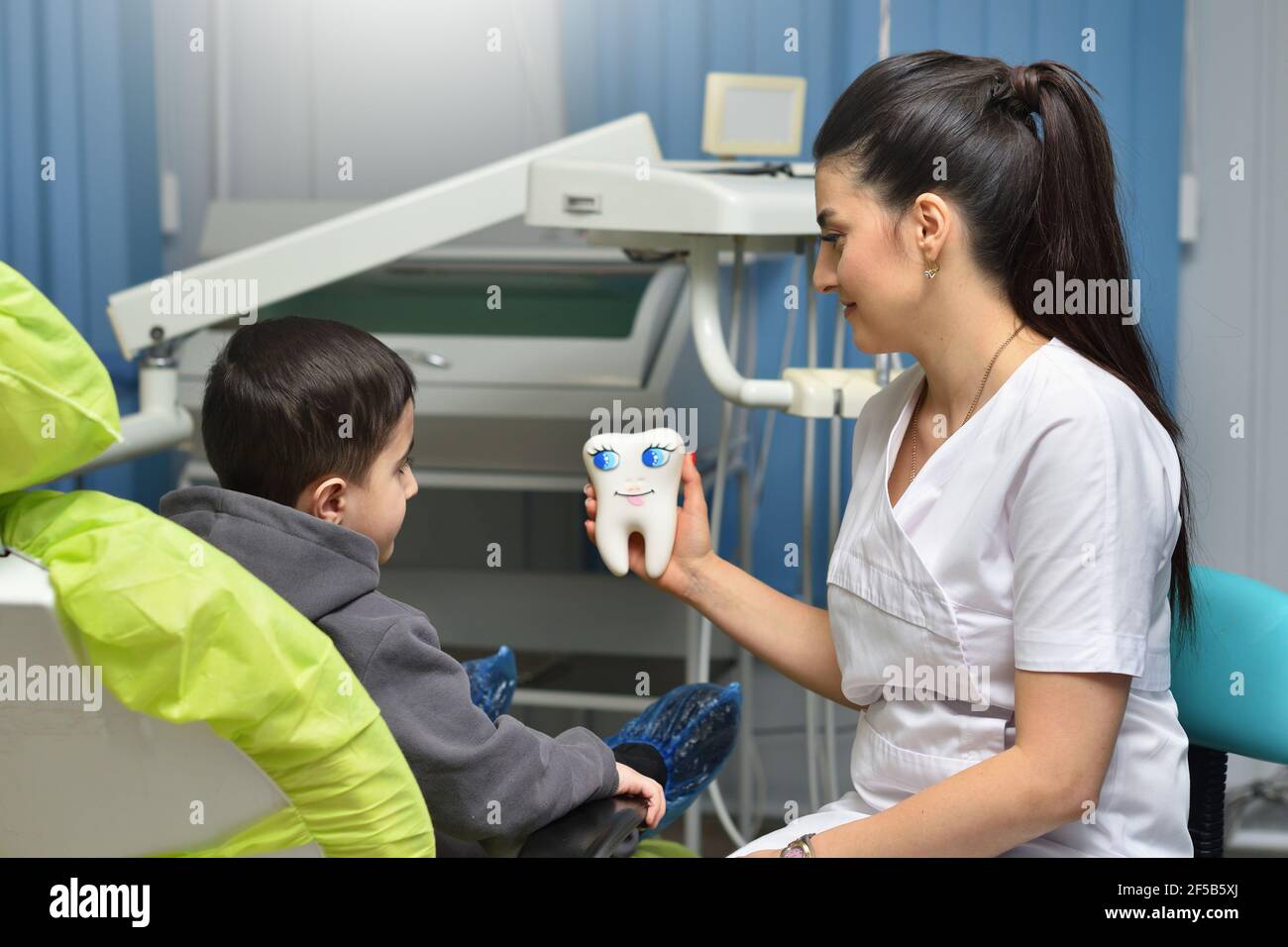 Donna dentista calma un bambino giù prima del trattamento dentale e. gli mostra un grande dente Foto Stock