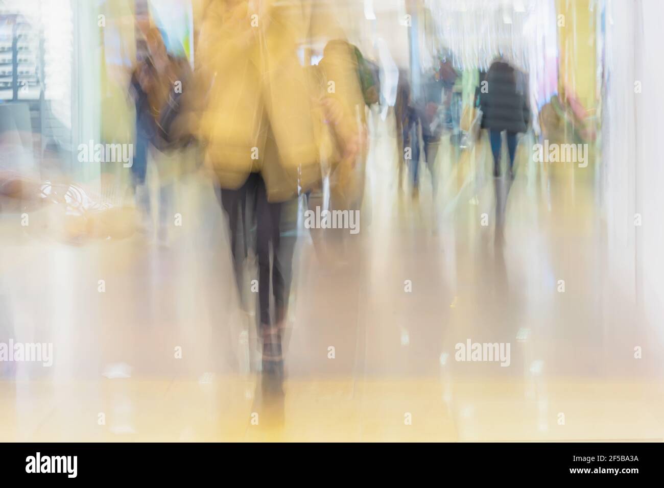 Silhouette astratta di persona in primo piano giacca gialla, sfondo. Movimenti sfocati hanno offuscato i giovani che camminavano nel centro commerciale Foto Stock