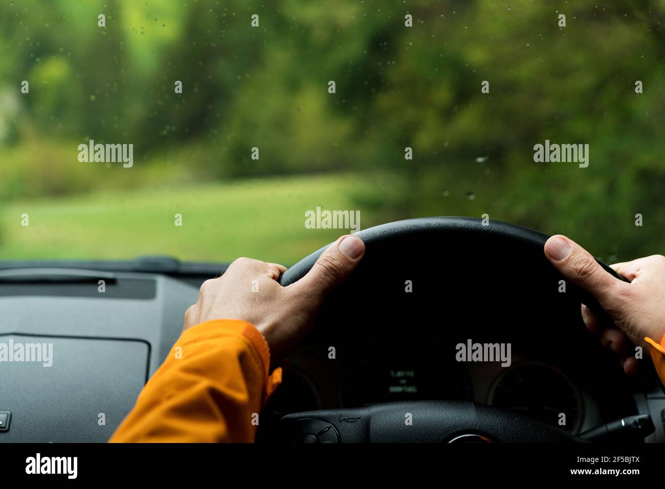 Primo piano immagine delle mani del conducente sul volante guida di una moderna auto fuoristrada con guida a destra sulla strada di campagna forestale verde di montagna. Insid Foto Stock
