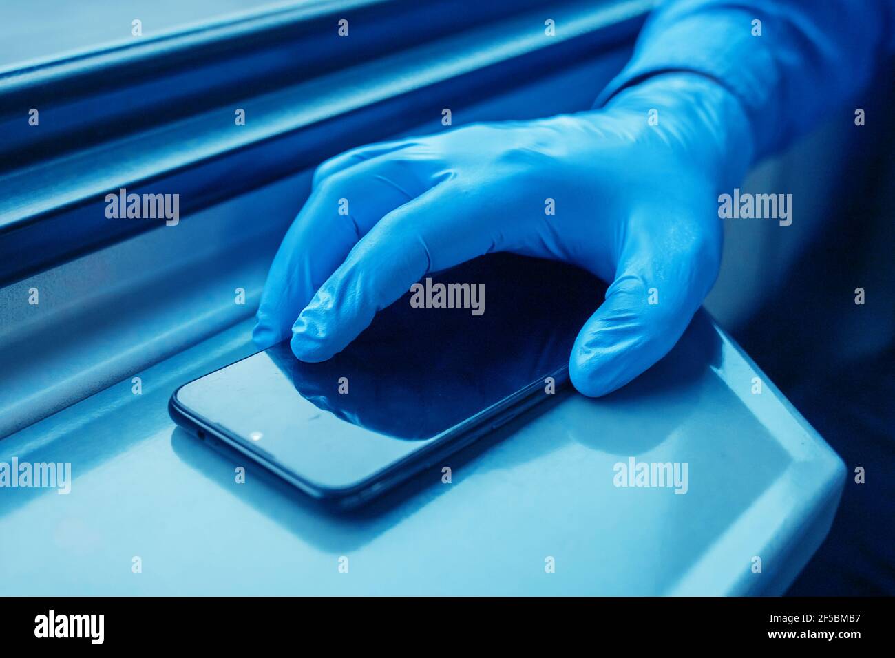La mano di un uomo in guanti medici protettivi prendere un telefono cellulare. Foto Stock